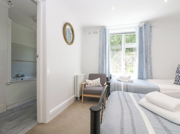 A bedroom with a bed, a chair, a radiator, and a window with curtains. - Godrevy (Penzance)