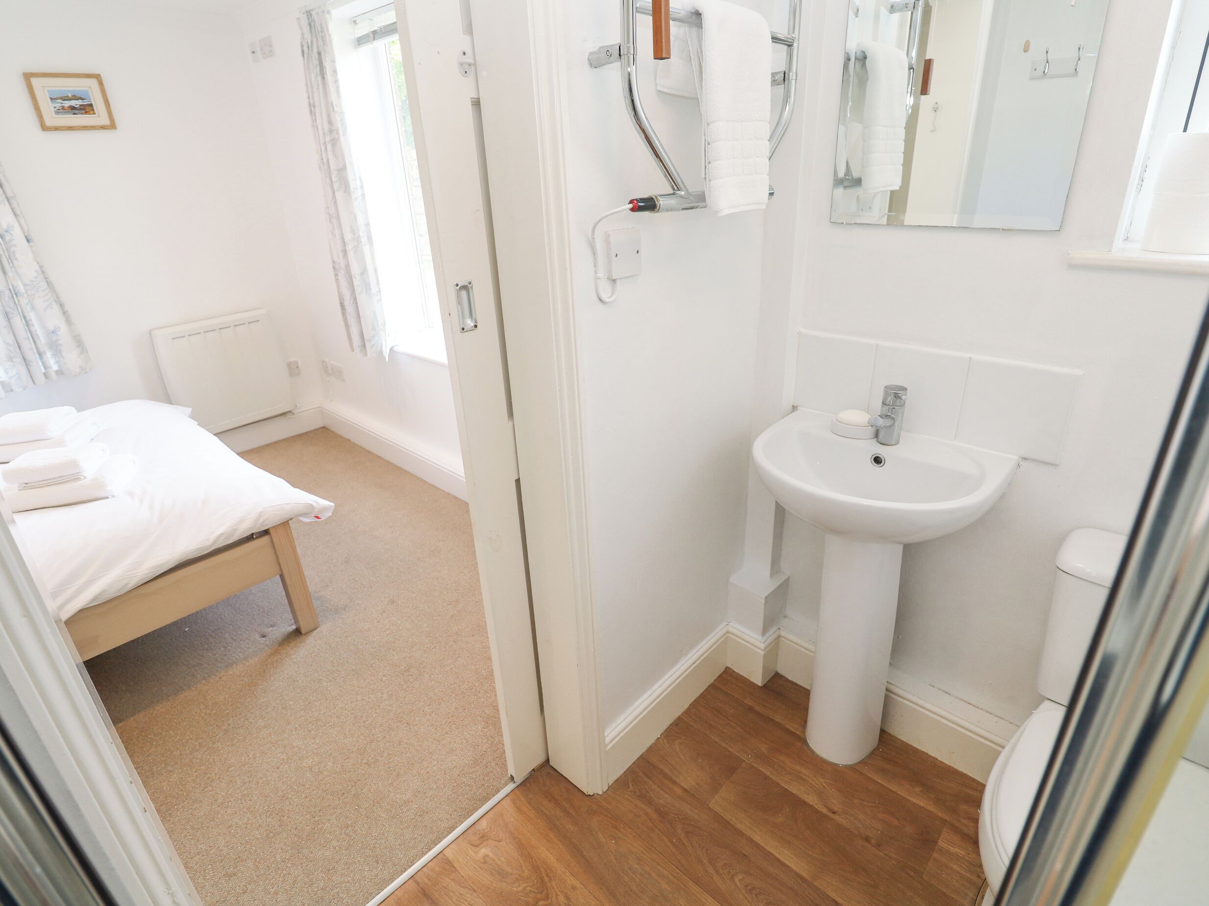 Une pièce propre et bien éclairée, avec un lit, un lavabo blanc et un miroir.