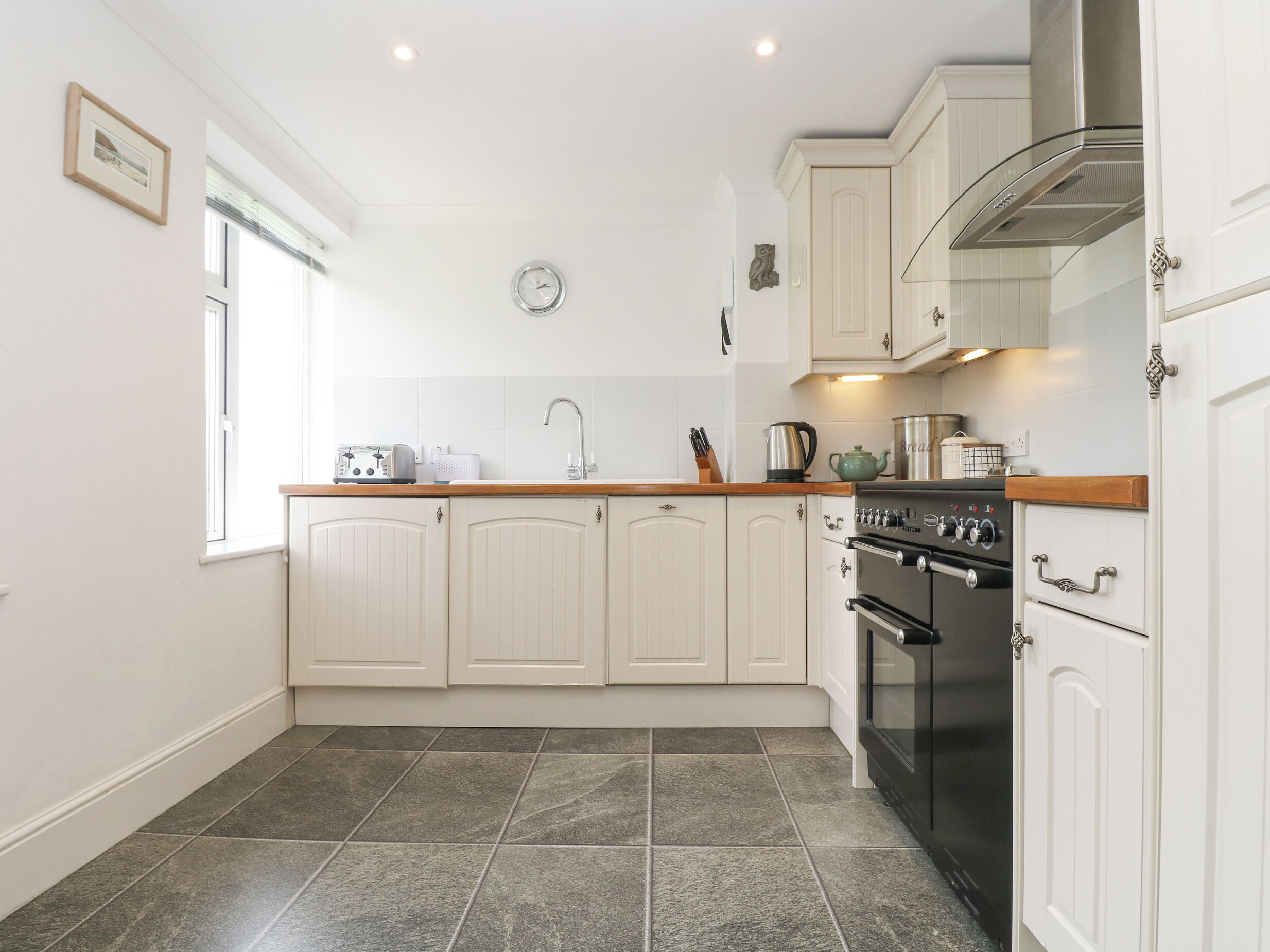 A kitchen with white cabinets, a black oven, and a window with blinds.