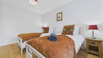 A hotel room with two beds, a wooden floor, a red lamp on the nightstand, and a framed picture on the wall.