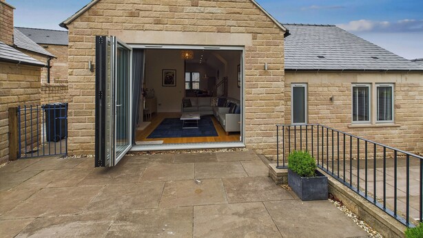 A stone building with a triangular roof, a glass door entrance, and a small garden area with a potted plant. - Oakwood Lodge (Matlock)