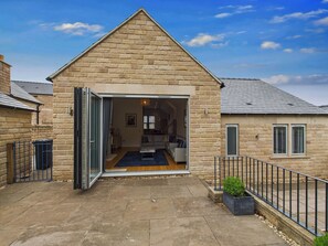 A stone building with a triangular roof, a glass door entrance, and a small garden area with a potted plant. - Oakwood Lodge (Matlock)