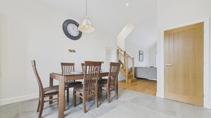A dining area with a wooden table and chairs, a wall clock, and a staircase leading to an upper level. - Oakwood Lodge (Matlock)