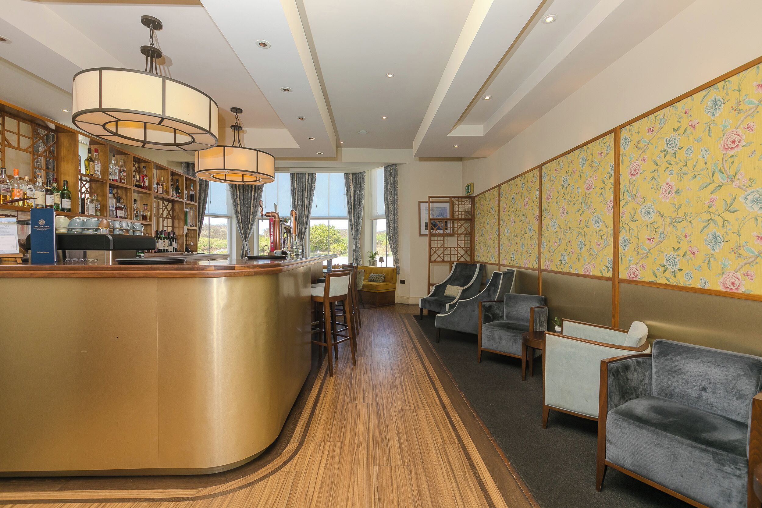 A bar area with a wooden counter, bar stools, and a seating area with armchairs and a sofa.