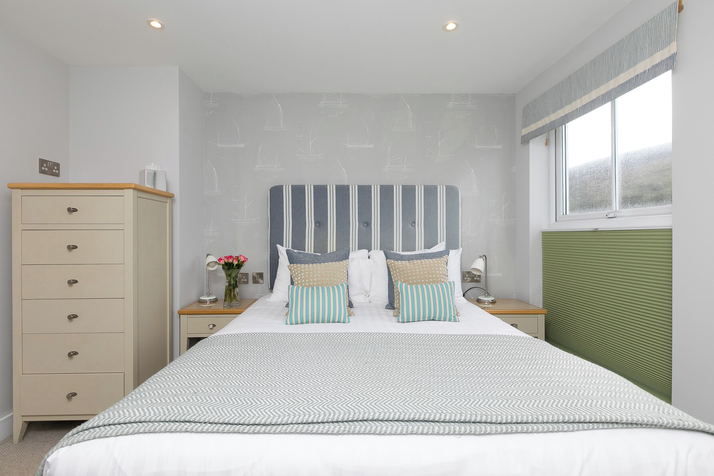 A bedroom with a bed, a nightstand, a dresser, and a window with blinds.