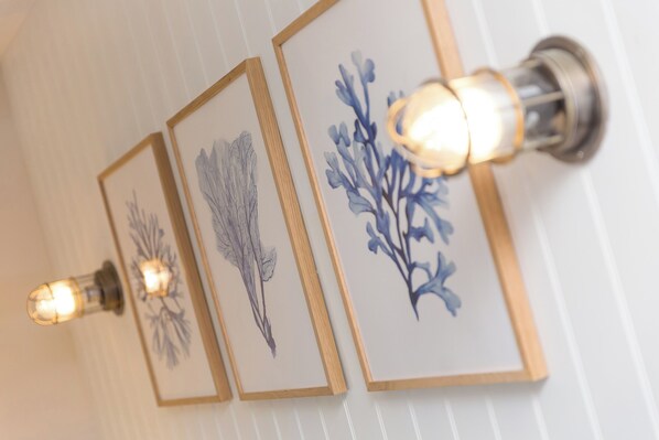 Three framed botanical illustrations on a wall, each illuminated by a light fixture. - Guinevere (Helston)