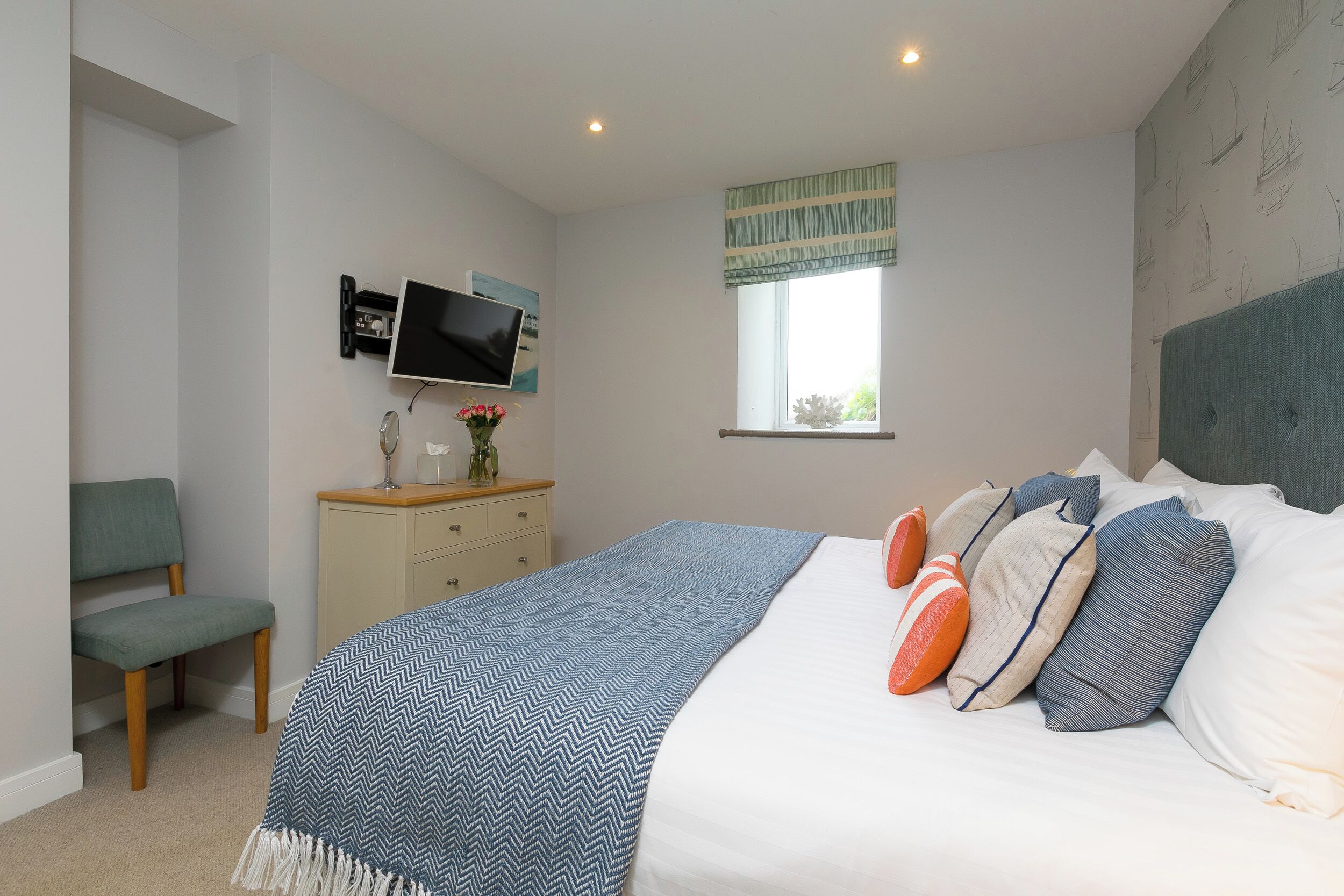 A bedroom with a bed, a TV mounted on the wall, a window with a view, a chair, and a dresser.