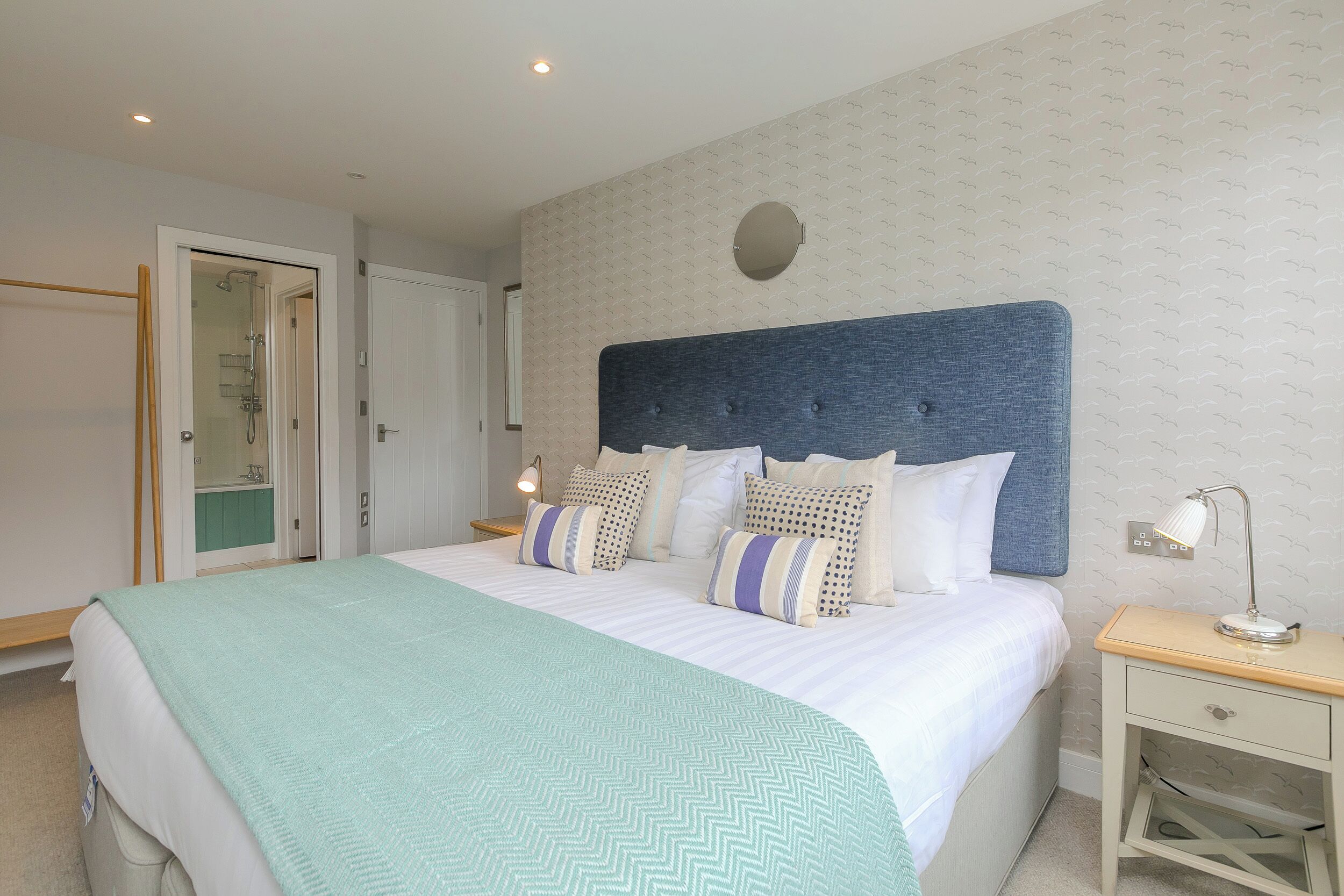 A neatly made bed with a blue headboard, a bedside lamp, and a small bedside table.