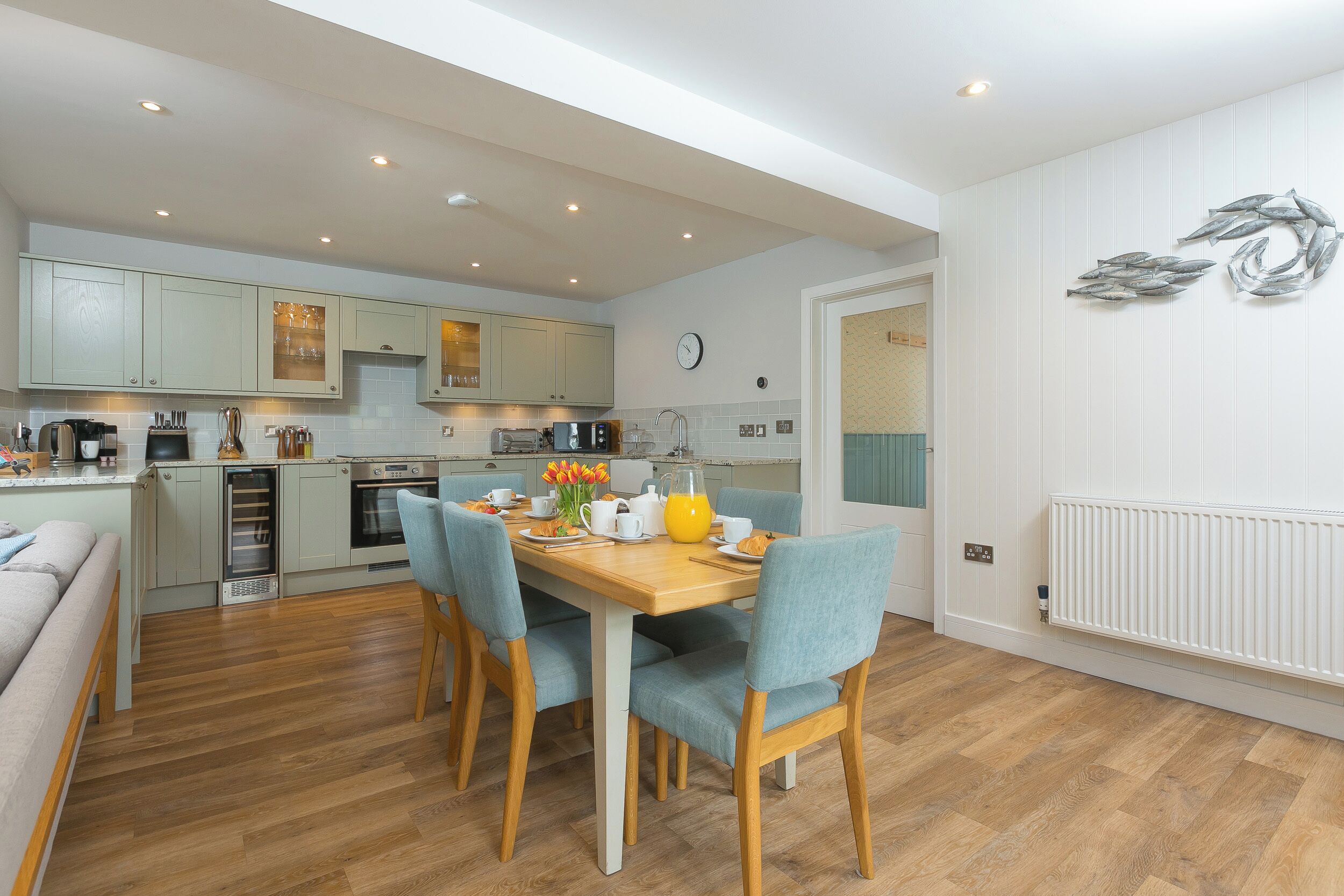 A modern kitchen with light-colored cabinets, a dining table with chairs, and a breakfast setup.