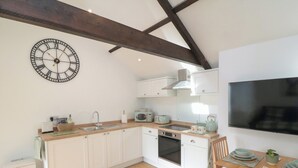 A modern kitchen with white cabinets, a wooden ceiling, a built-in oven, a microwave, and a large clock on the wall.