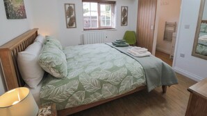A bedroom with a bed, a window with blinds, a radiator, a green chair, and a wooden wardrobe.