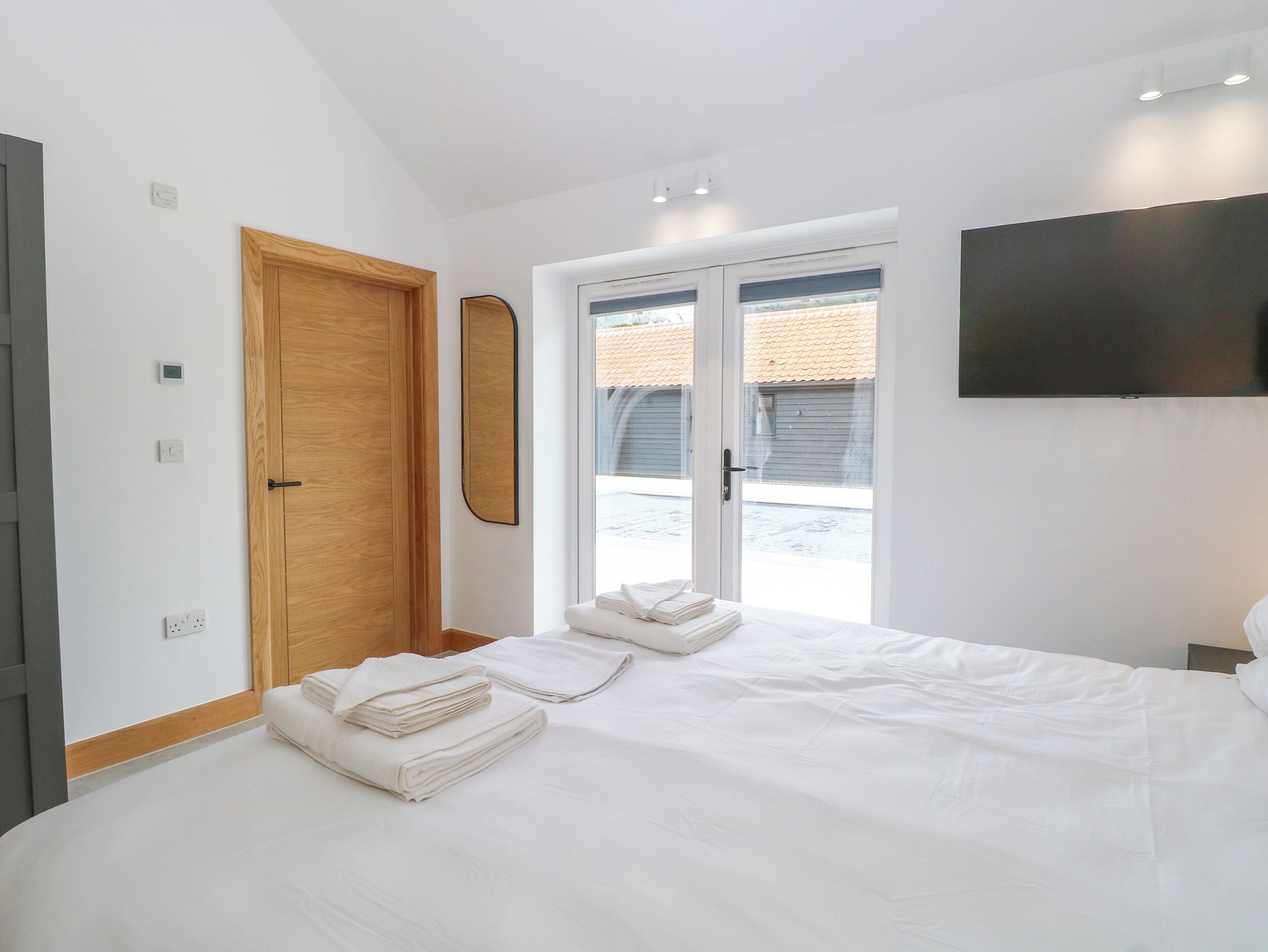 A modern bedroom with a large bed, a wooden door, a mirror, and a TV on the wall.