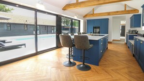A modern kitchen with blue cabinets, a wooden ceiling, and a large island with bar stools. - County Farm Barn (Norwich)
