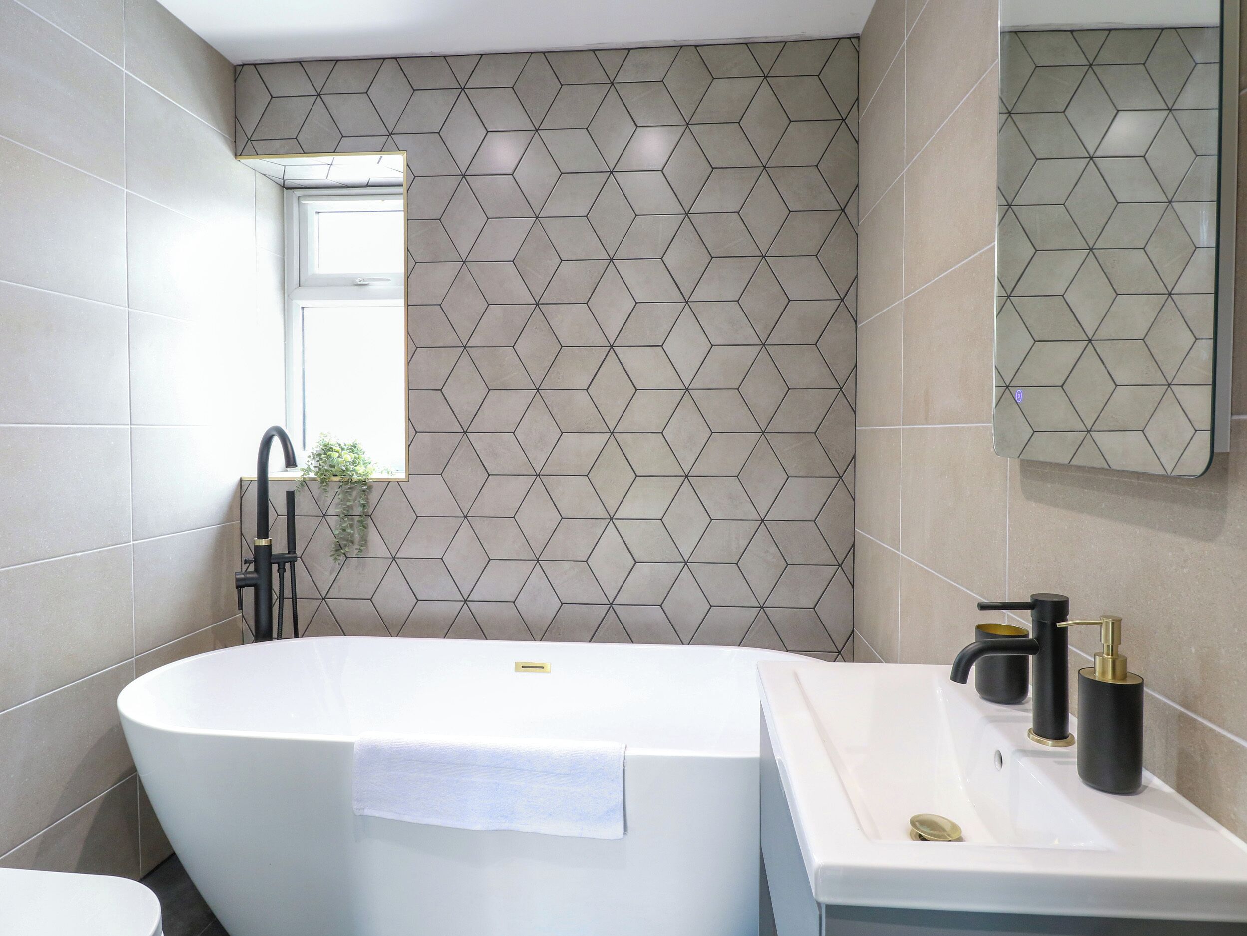 A modern bathroom with a freestanding bathtub, a sink with a gold faucet, and a geometric-patterned wall.