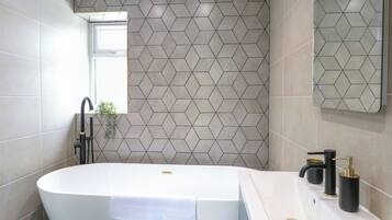 A modern bathroom with a freestanding bathtub, a sink with a gold faucet, and a geometric-patterned wall.