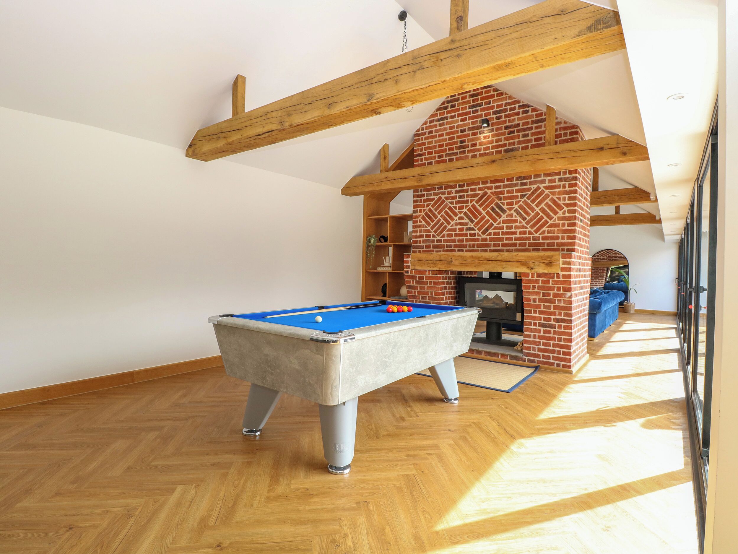 A pool table in a room with wooden beams and a brick fireplace.