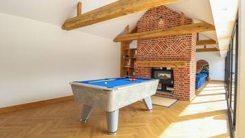 A pool table in a room with wooden beams and a brick fireplace.