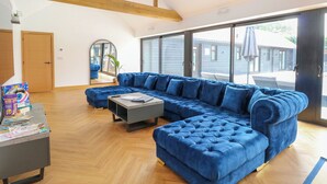 A spacious living room with a large blue sectional sofa, a coffee table, and a wooden floor. - County Farm Barn (Norwich)
