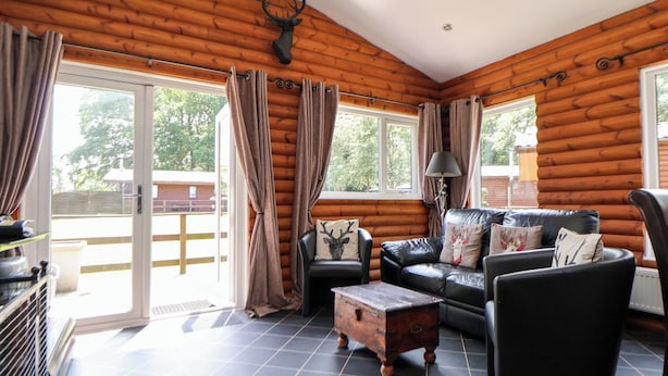 L’intérieur d’une cabane en rondins, avec une cheminée, des canapés en cuir et une tête de cerf accrochée au mur.