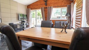 Une table à manger en bois avec quatre chaises, un téléviseur et une cheminée, le tout dans l’intérieur d’un chalet en rondins.