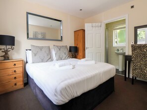 A bedroom with a large bed, a dresser, a mirror, a door, and a window. - The Fallows (Saint Asaph)
