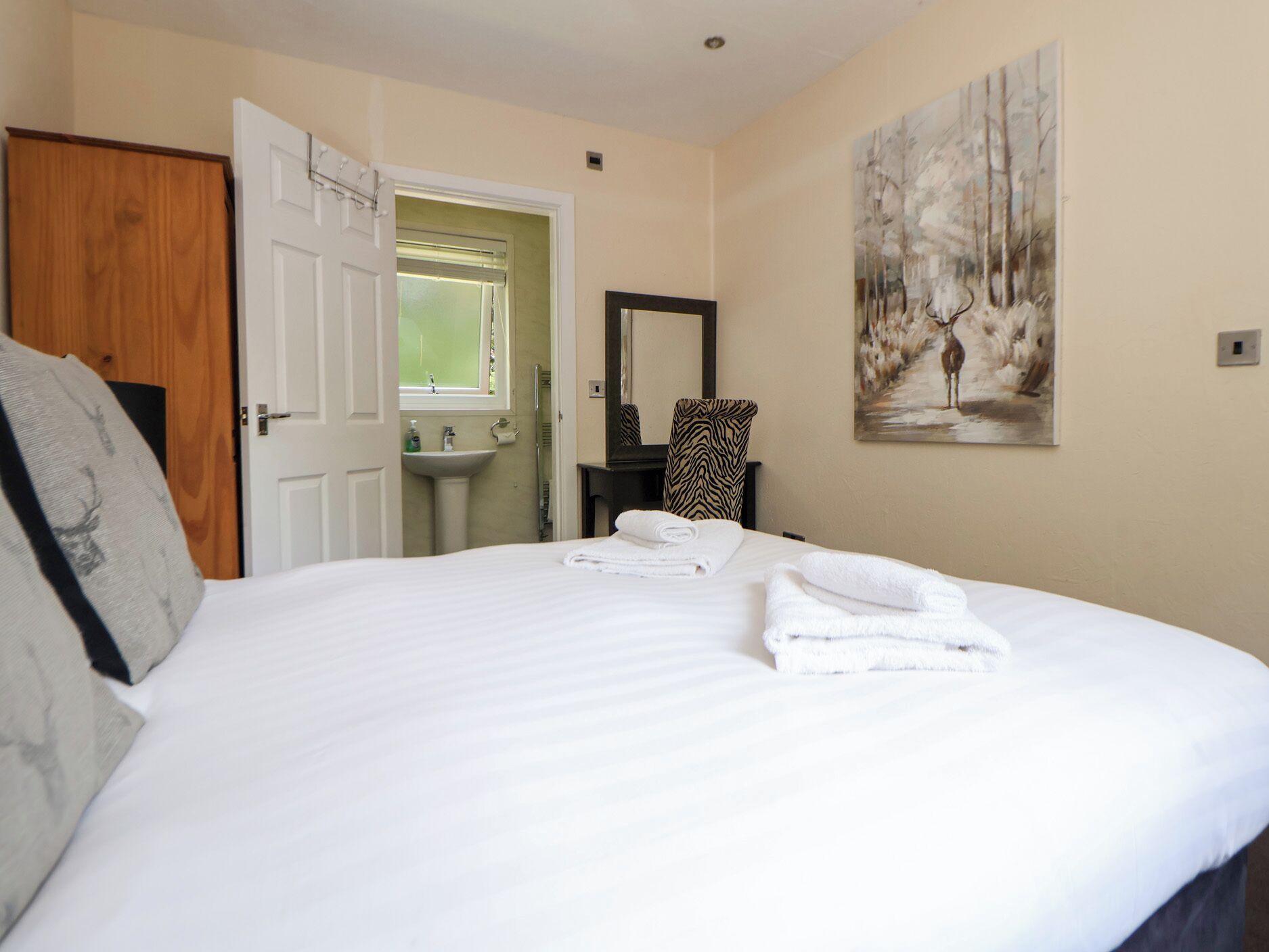 A hotel room with a bed, a bathroom, a zebra-patterned chair, and a painting on the wall.