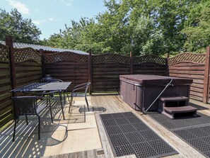 An outdoor patio with a table and chairs, a hot tub, and a wooden fence. - The Fallows (Saint Asaph)