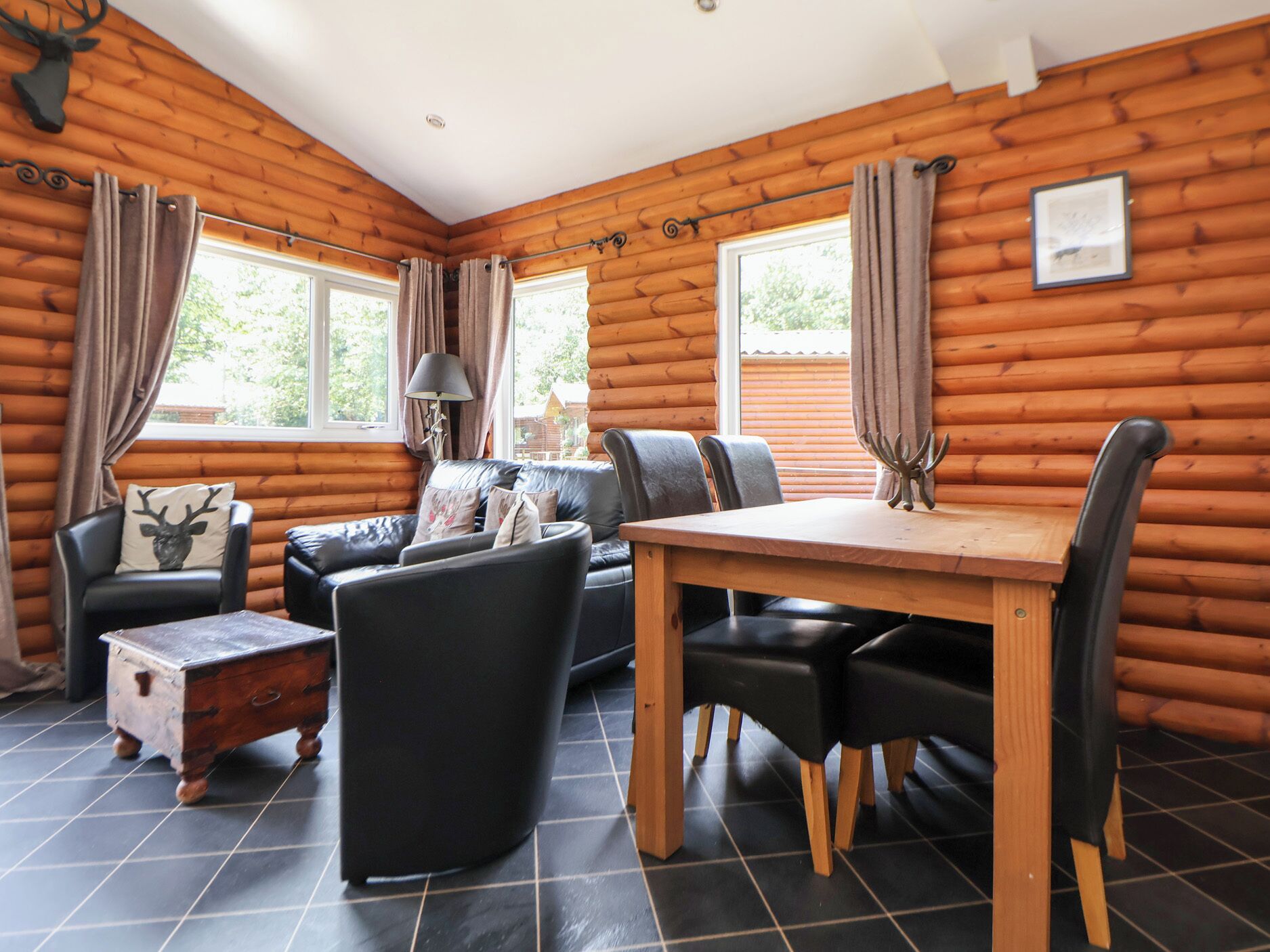 A log cabin interior with a dining table, chairs, a sofa, and a small wooden chest.