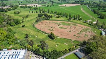Vogelperspektive eines Golfplatzes mit einer großen, zentralen Fläche, umgeben von Wohngebäuden und Grünflächen.