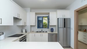A modern kitchen with white cabinets, a stainless steel refrigerator, and a window with blue shutters.