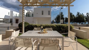 An outdoor patio with a white table and chairs, a pergola overhead, and a view of modern buildings in the background.