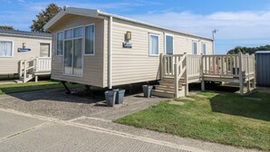 Une maison mobile dotée d’un porche à l’avant, d’une petite terrasse et d’une fenêtre avec un rideau.
