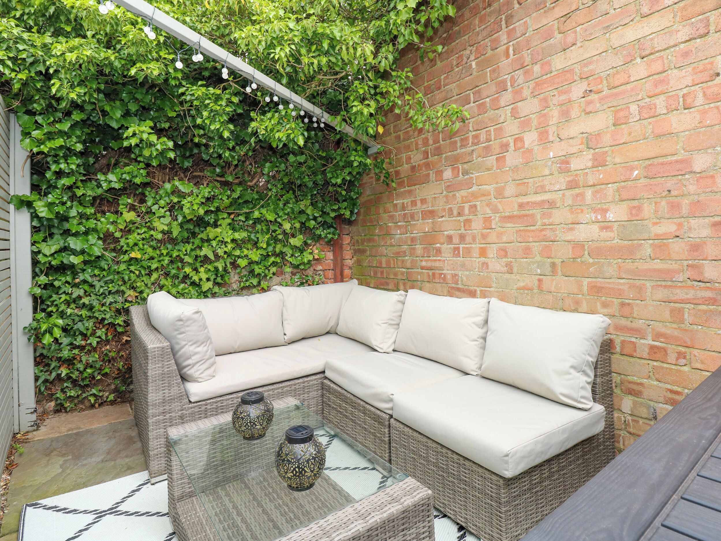 A wicker sectional sofa with cushions, a glass-top coffee table, and two decorative vases.