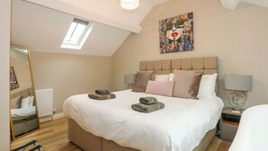 A bedroom with a large bed, a skylight, a mirror, a painting, and a bedside table with a lamp. - Daisy's Place (Fakenham)
