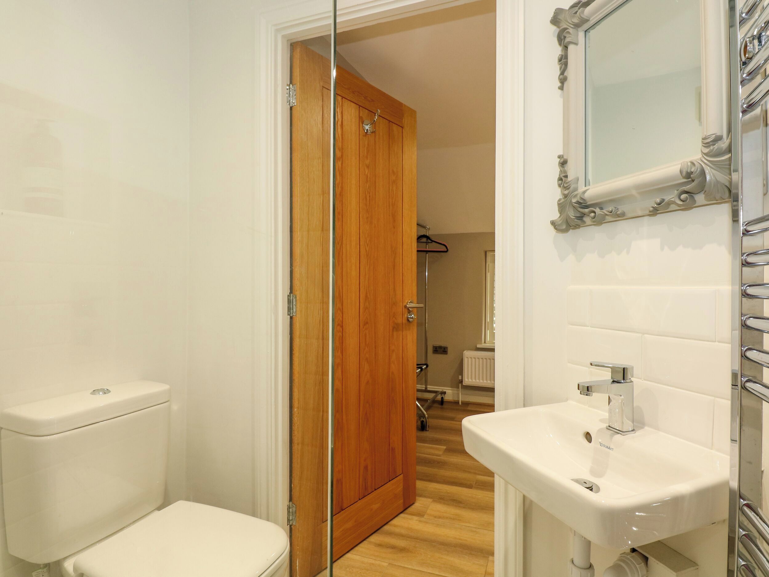 A bathroom with a toilet, a wooden door, a sink, and a mirror.