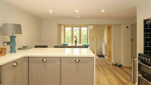A modern kitchen with a central island, white cabinetry, and a view to the outside. - Daisy's Place (Fakenham)