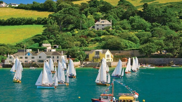 A coastal scene with sailboats on the water, a ferry, and houses on a hillside. - Leylands (Salcombe)