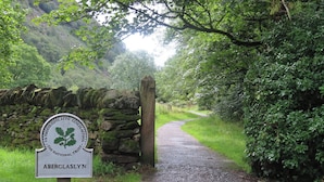 A sign for Aberglasyn, a National Trust property, with a stone wall and a gravel path leading through a wooded area. - Cottage on the Green (Caernarfon)