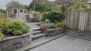 A backyard with a stone patio, a wooden fence, and various plants. - Cottage on the Green (Caernarfon)