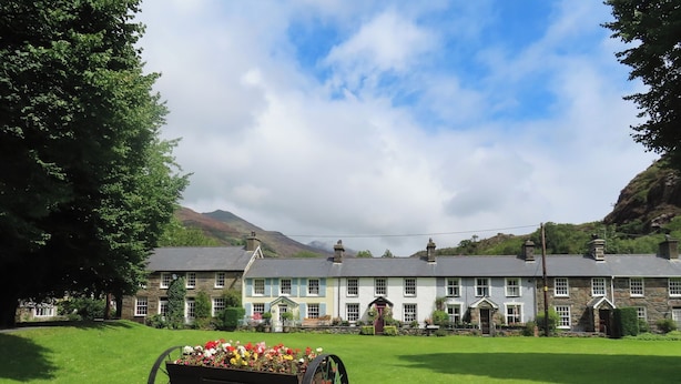 A traditional stone building with a large lawn in front, a flower cart, and mountains in the background. - Cottage on the Green (Caernarfon)
