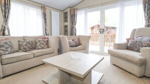 A spacious living room with a beige sofa set, a wooden coffee table, and a sliding glass door leading to an outdoor area. - Tawny Owl Lodge (Windermere)