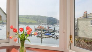 Vista desde una ventana a un puerto con barcos, una colina cubierta de hierba y un edificio de fachada de piedra.