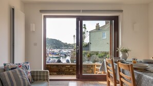 Un salón acogedor con un sofá, una mesa de comedor para dos personas y vista a un puerto deportivo a través de un ventanal corredero.