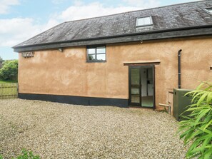 A single-story building with a gravel driveway, a door with glass panels, and a small window. - Ixworth Cottage (Ottery St Mary)