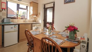 A compact kitchen with a dining area, a clock, and a painting of swans. - Fatima (Burnham-on-Sea)