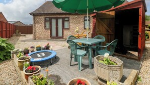 A patio with a table and chairs, a trampoline, and potted plants. - Fatima (Burnham-on-Sea)