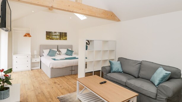 A modern bedroom with a bed, bedside tables, a grey sofa, and a wooden coffee table. - 2 Welford Barns (Fordingbridge)