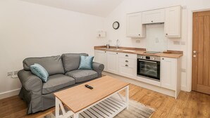 A compact living space with a kitchenette, a grey sofa, a wooden coffee table, and a wooden door. - 2 Welford Barns (Fordingbridge)