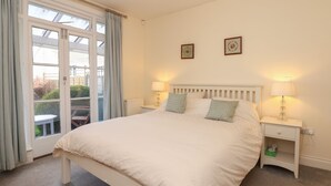 Une chambre avec un grand lit, deux tables de chevet avec des lampes, une fenêtre avec des rideaux et deux tableaux encadrés accrochés au mur.