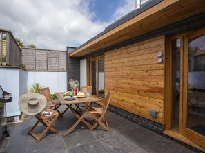 A patio with a wooden table and chairs, a grill, and a stone floor. - 2 Dart (Totnes)